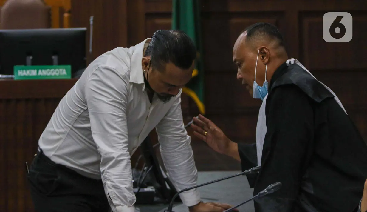 Terdakwa musisi I gede Ari Astina atau Jerinx berbincang dengan kausa hukumnya saat mengikuti sidang tuntutan di PN Jakarta Pusat, Jakarta, Jumat (18/2/2022). Jerinx dituntut dua tahun penjara dan denda Rp50 juta subsider dua bulan kurungan. (Liputan6.com/Herman Zakharia)