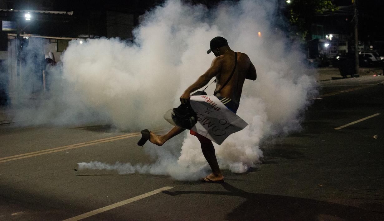 Seorang penduduk favela Cidade de Deus (Kota Tuhan) menendang tabung gas air mata yang ditembakkan oleh polisi selama protes di kota kumuh di Rio de Janeiro, Brasil, pada 7 Agustus 2023. (AFP/Tercio Teixeira)