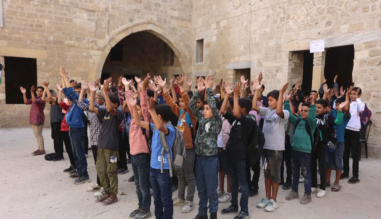Anak-anak Palestina berdiri di halaman sekolah bersejarah "Al-Kamaliya al-Othmanya" saat mereka berolahraga sebelum masuk sekolah di Kota Tua Gaza yang menjadi bagian dari inisiatif sukarelawan yang diorganisir oleh para guru pengungsi, di Kota Gaza pada 2 November 2025. Banyak di antaranya kini dialihfungsikan menjadi tempat penampungan darurat yang menampung puluhan ribu pengungsi. (Omar AL-QATTAA/AFP)