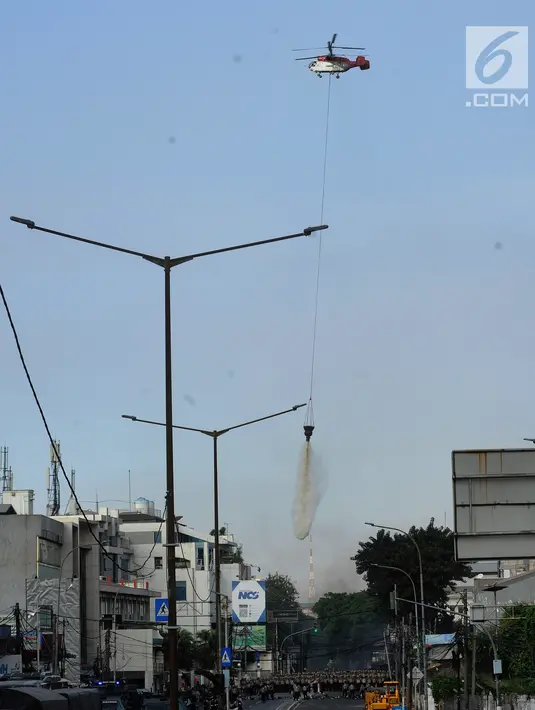 Helikopter water bombing menyiramkan air ke arah ban yang dibakar massa di kawasan Slipi, Jakarta, Rabu (22/5/2019). Air dijatuhkan dari udara ke arah api yang berasal dari ban bekas. (merdeka.com/Arie Basuki)