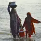 Wanita yang terkena banjir membawa air minum dalam wadah setelah melarikan diri dari banjir yang melanda rumah mereka setelah hujan lebat di daerah Sohbatpur di distrik Jaffarabad di provinsi Balochistan (29/8/2022). (AFP/Fida Hussain)