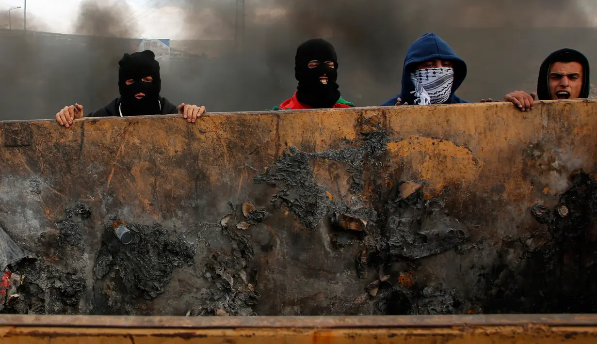 Demonstran Palestina mendorong sebuah wadah sampah untuk menutup jalan saat terjadi bentrokan di kota Ramallah, Palestina (16/3). (AFP Photo/Abbas Momani)