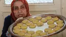 Perempuan Palestina dengan mengenakan sarung tangan menunjukkan biskuit tradisional yamg disiapkan menjelang Idul Fitri di sebuah rumah di kota tua Hebron, Tepi Barat yang diduduki, Selasa (19/5/2020). Biskuit-biskuit itu akan dijual secara online guna menjaga jarak saat Covid-19. (HAZEM BADER/AFP)