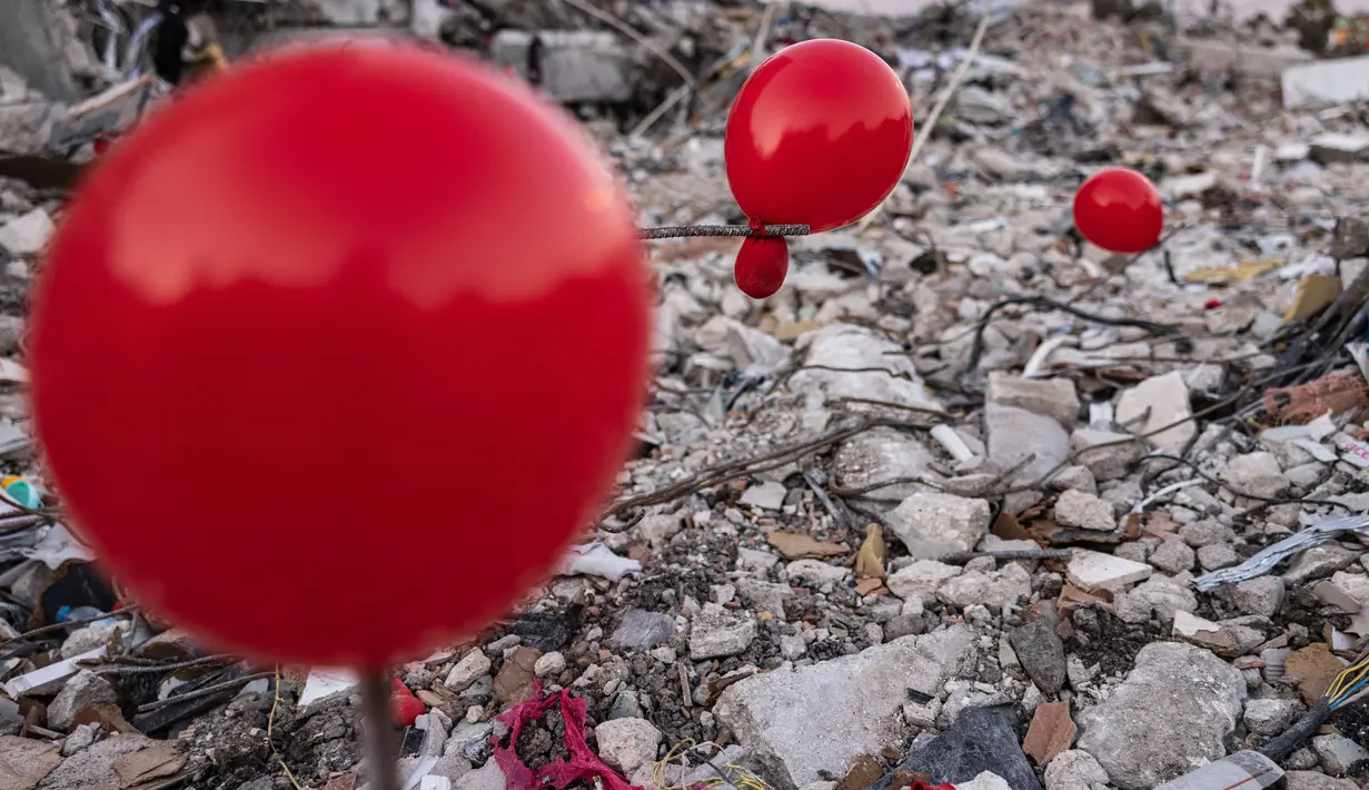 Balon yang tergantung di puing-puing bangunan yang runtuh di Antakya, Turki selatan, menyusul gempa berkekuatan 6,4 yang melanda pada 20 Februari, dua minggu setelah gempa berkekuatan 7,8 melanda dekat Gaziantep dan telah menewaskan lebih dari 44.000 orang.  Di sisi jalan yang sibuk di Antakya, puluhan balon merah berkibar, bergelantungan di reruntuhan.  (AFP/Sameer Al-Doumy)