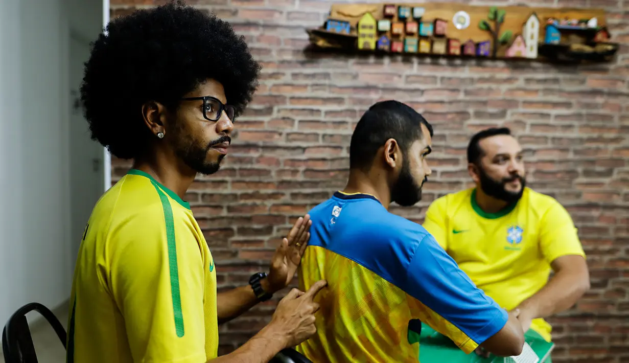 Helio Fonseca (kanan) dan Vinicius Alves (kiri) membantu teman mereka yang tuli dan buta Carlos Junior (tengah) dengan play-by-play pertandingan sepak bola Grup G Piala Dunia antara Brasil dan Swiss di Osasco, Sao Paulo, Brasil, 28 November 2022. Fonseca dan Alves menggunakan meja taktil dan sentuhan pada tubuh tunanetra dan tunarungu untuk menunjukkan kepada mereka pergerakan bola dan para pemain selama pertandingan sepak bola. (AP Photo/Marcelo Chello)