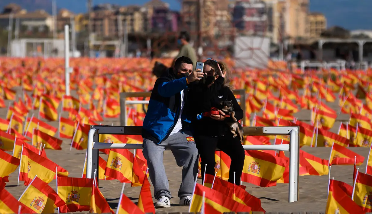Sepasang suami istri ber-wefie saat mereka duduk di antara ribuan bendera Spanyol yang mewakili korban COVID-19, di pantai Patacona, Valencia pada Minggu (4/10/2020). Virus corona di Spanyol sejauh ini telah merenggut lebih dari 32.000 nyawa dan 790.000 kasus terkonfirmasi. (Jose Jordan / AFP)