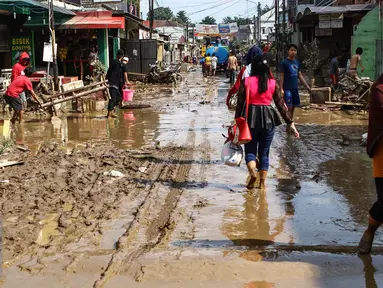 Warga melintas di sepanjang jalan yang dipenuhi lumpur di komplek Pondok Gede Permai Jatiasih, Bekasi, Jumat (22/04). Banjir yang telah merendam ratusan rumah warga mengakibatkan air lumpur mengendap. (Liputan6.com/Fery Pradolo)
