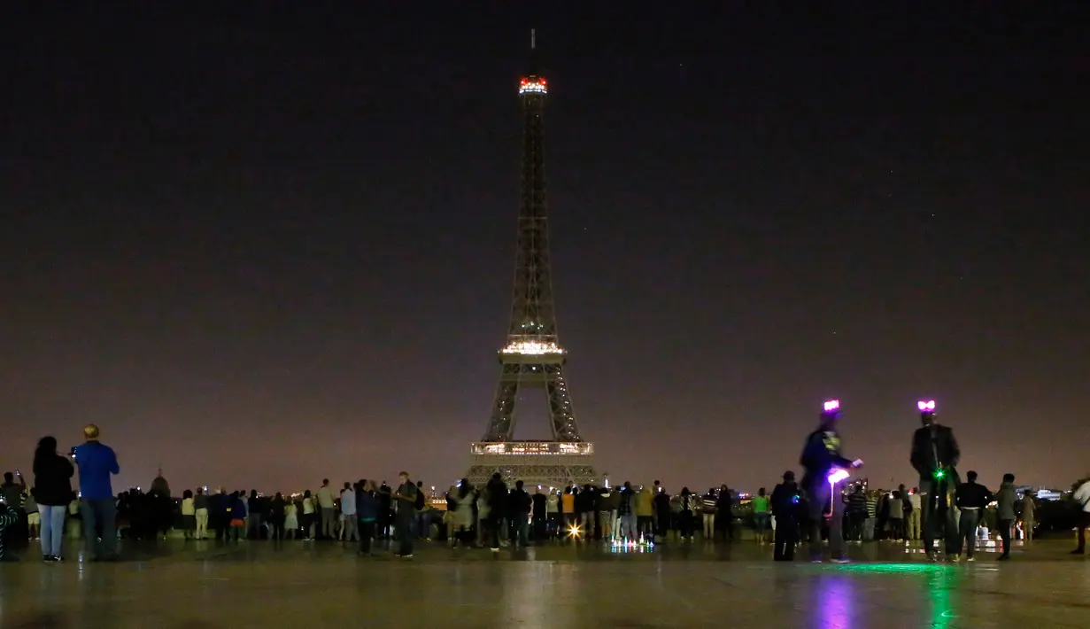 Pengunjung berkumpul di alun-alun Trocadero saat lampu Menara Eiffel di Paris, dipadamkan, Rabu (24/5) dini hari. Hal itu sebagai bentuk penghormatan dan duka cita atas serangan bom pada konser Ariana Grande di Manchester, Inggris (AP Photo/Francois Mori)