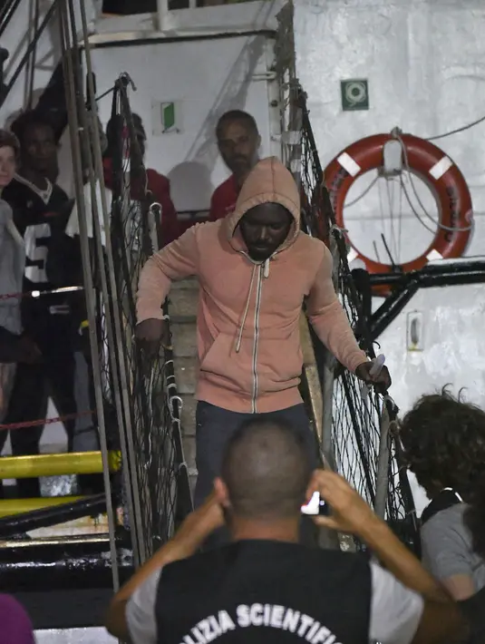 Imigran turun dari kapal penyelamat Open Arms di Lampedusa, Italia (20/8/2019). Jaksa penuntut Italia Luigi Patronaggio telah memerintahkan penyitaan sebuah kapal penyelamat migran dan evakuasi langsung lebih banyak lagi dari 80 migran yang tersisa di kapal. (AP Photo/Salvatore Cavalli)