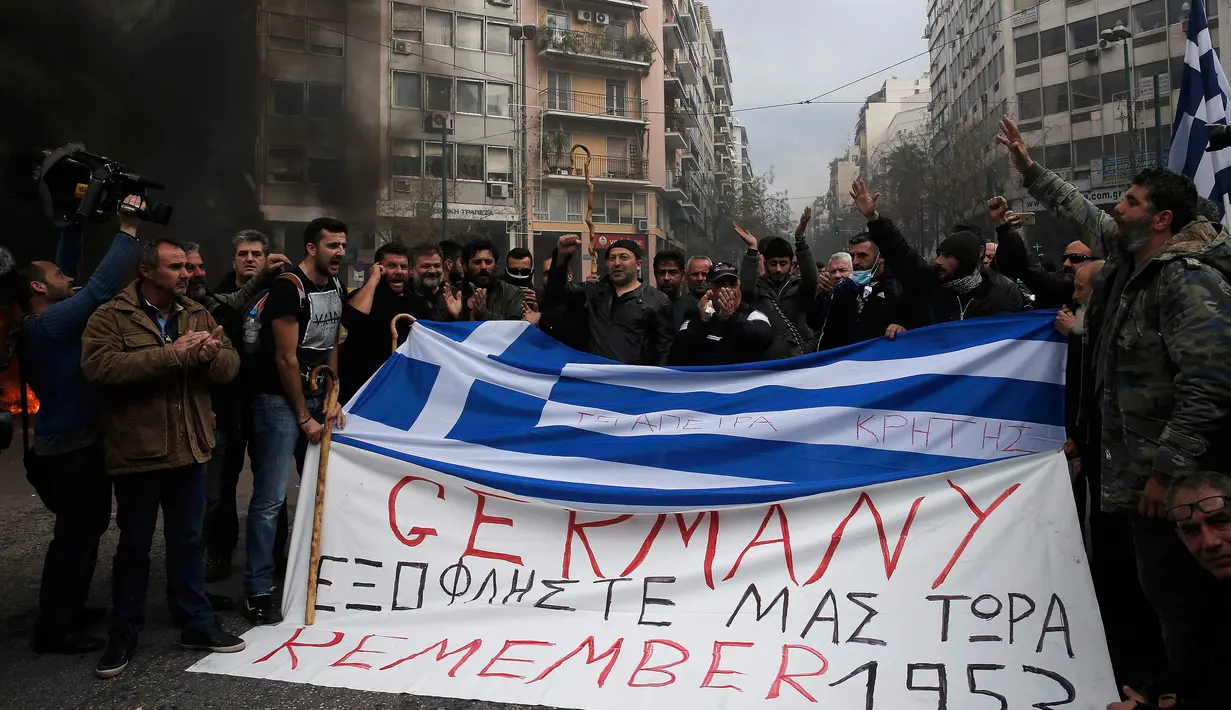 Ratusan Petani membawa bendera Yunani bertuliskan "Germany pay us back now" selama protes petani terhadap perubahan peraturan pensiun yang direncanakan di luar Kementerian Pertanian, Athena, Yunani, Jumat (12/2). (REUTERS/Alkis Konstantinidis)	