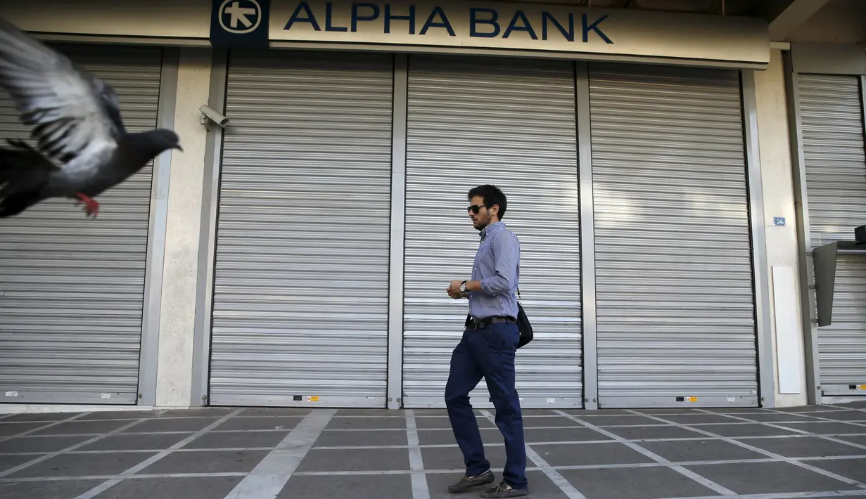 Seorang pria berjalan melintasi sebuah bank yang berhenti beroperasi di Athena, Yunani, (29/6/2015). Seperti dikutip BBC, penarikan uang pun dibatasi hanya 60 euro per hari. (REUTERS/Marko Djurica)