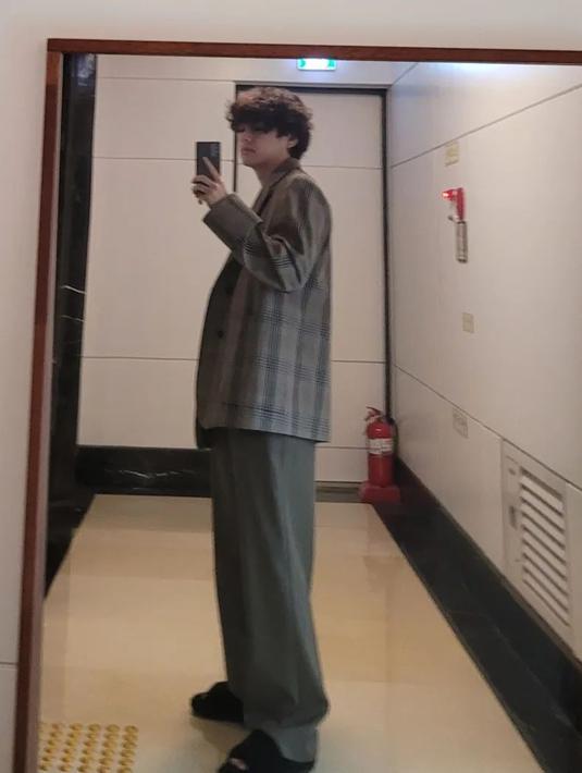 Busana setelan oversize yang digunakan oleh V saat melakukan mirror selfie ini membuat penampilannya semakin memesona. Dirinya pun terlihat menata rambut dengan cukup sederhana serta memakai sandal rumah berwarna hitam. (Liputan6.com/IG/@thv)