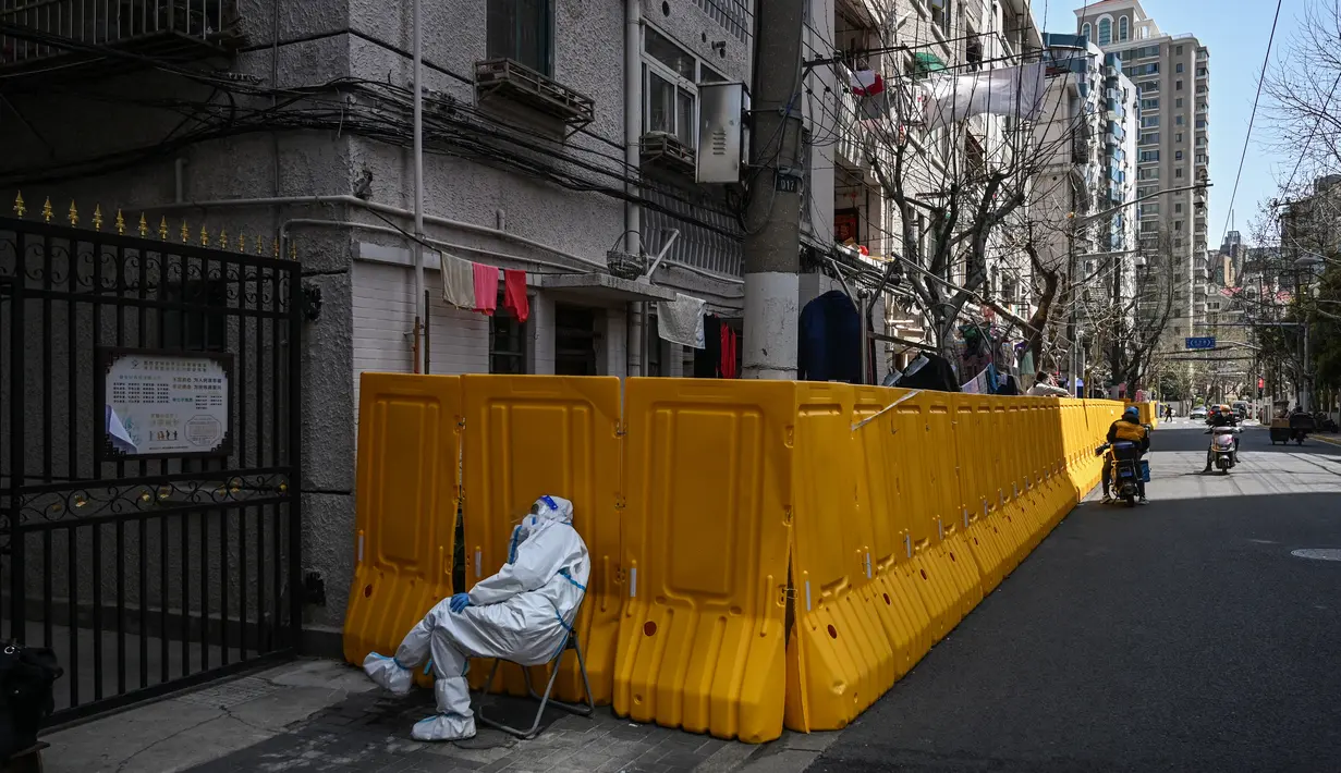 Seorang pekerja mengenakan pakaian pelindung menjaga pintu masuk ke lingkungan yang dikunci sebagai tindakan melawan virus corona Covid-19, di distrik Jing'an, di Shanghai (29/3/2022). (AFP/Hector Retamal)