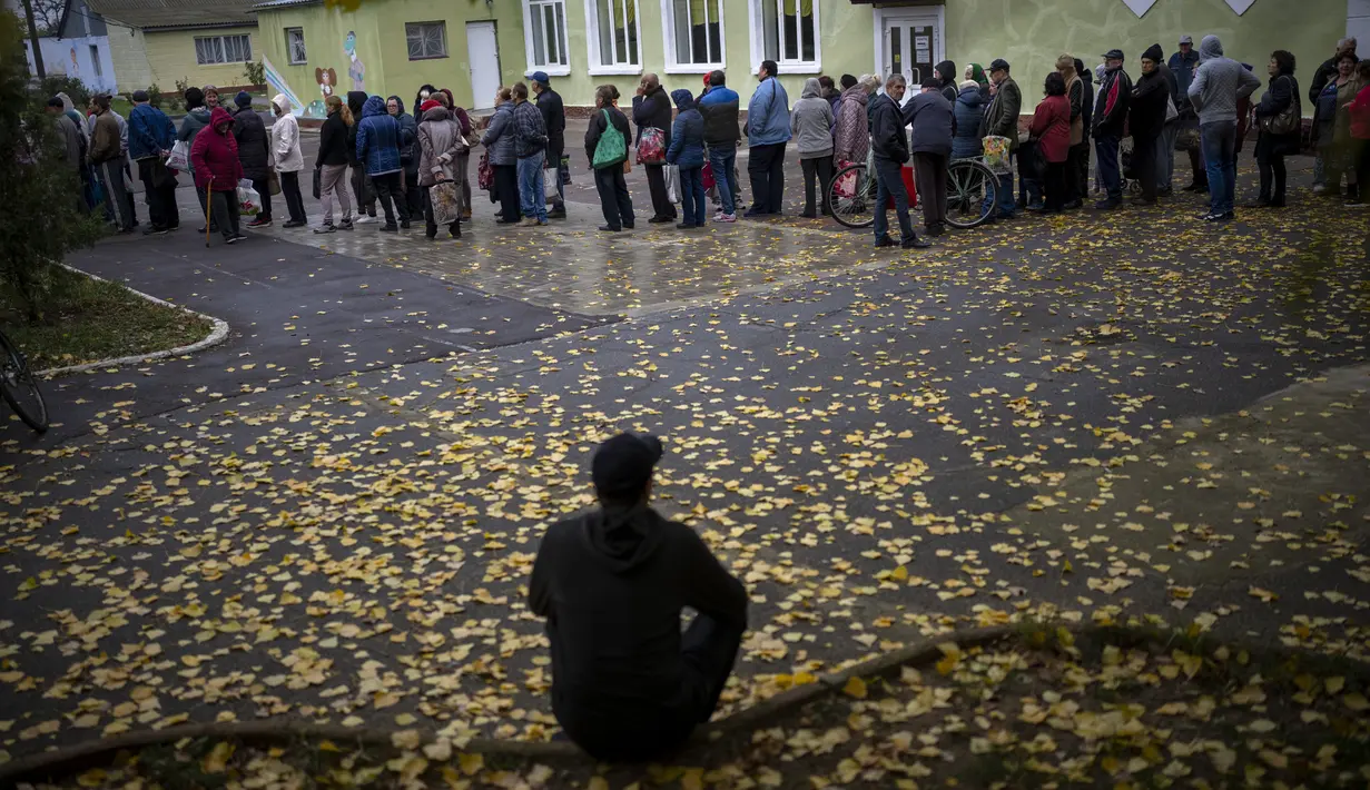 Seorang pria duduk saat orang-orang mengantre untuk menerima jatah roti setiap hari di sebuah sekolah di Mykolaiv, Ukraina, Selasa (25/10/2022). Antrean yang berada di jalanan Mykolaiv ini berbahaya karena dekat dengan garis depan dan sering terkena tembakan. (AP Photo/Emilio Morenatti)