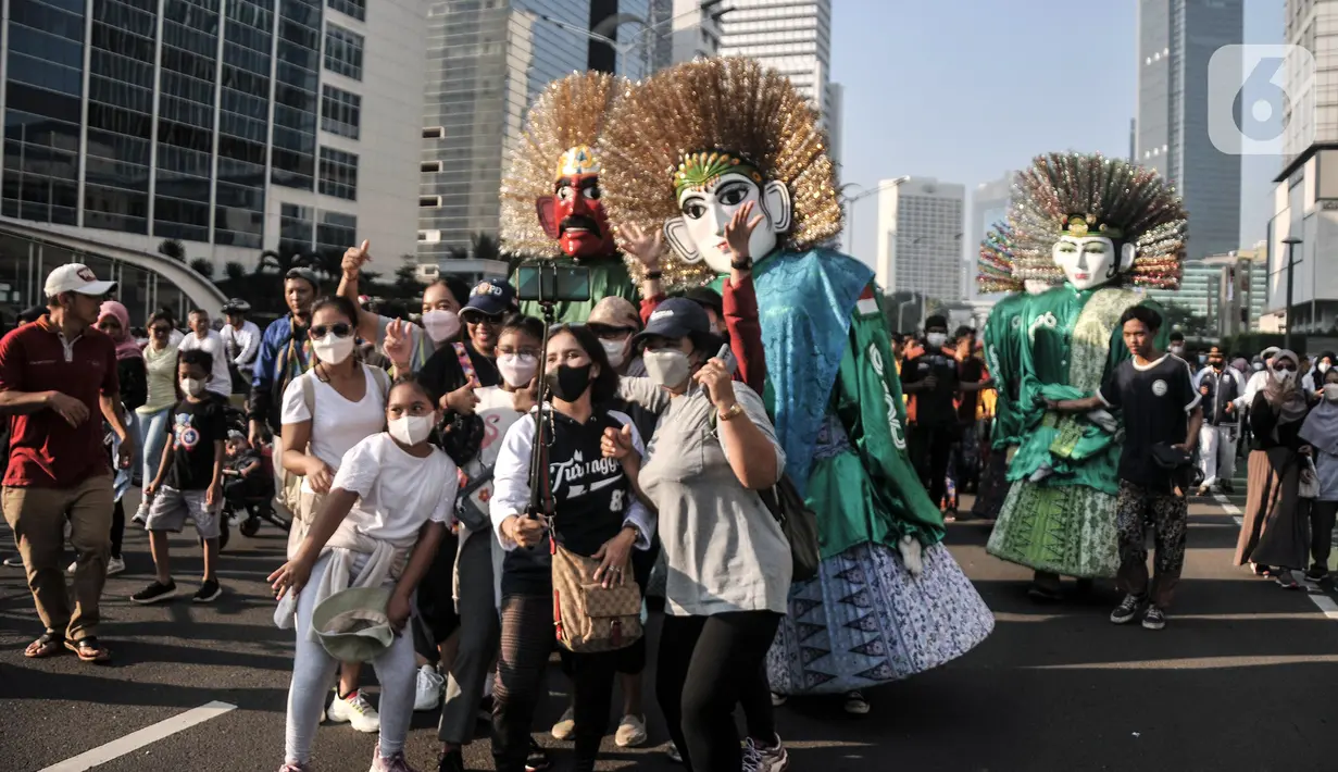 Warga berfoto dengan ondel-ondel yang tampil dalam pawai budaya dan kesenian Betawi saat Hari Bebas Kendaraan Bermotor (HBKB) atau car free day (CFD) di Jalan MH Thamrin, Jakarta, Minggu (19/6/2022). Pawai yang menampilkan berbagai budaya dan kesenian Betawi seperti ondel-ondel, tari topeng, serta tanjidor tersebut digelar dalam rangka menyambut HUT ke-495 DKI Jakarta. (merdeka.com/Iqbal S. Nugroho)