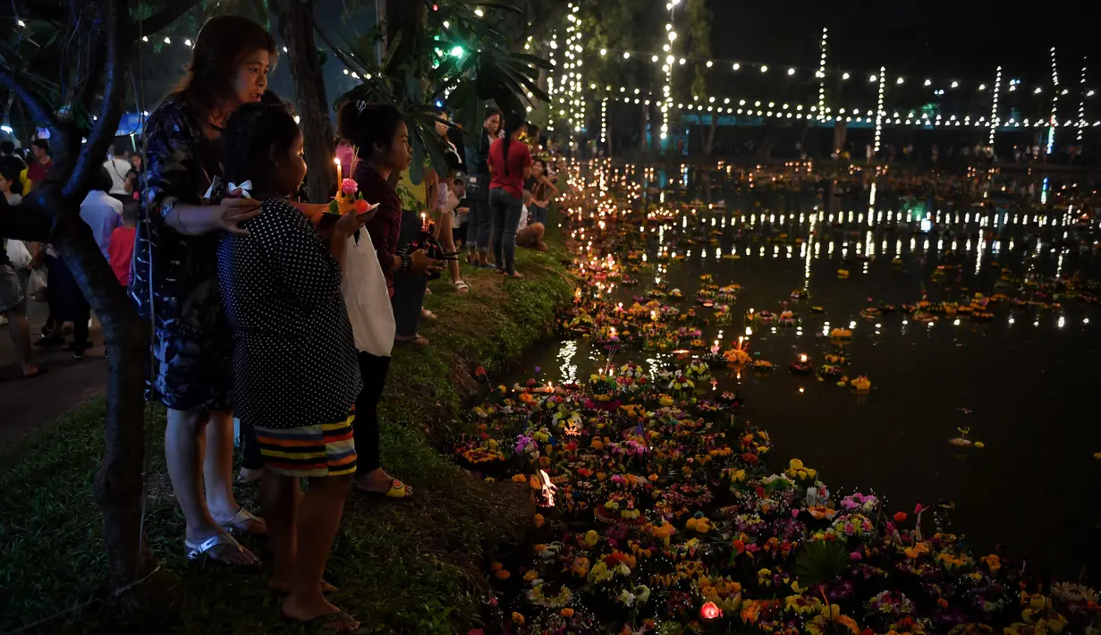 Seorang pria mengajak anaknya menghanyutkan 'krathong' untuk menandai festival Loy Krathong di sebuah danau di Bangkok, Senin (11/11/2019). Festival ini selalu dirayakan besar-besaran oleh warga Thailand, tak jarang turis mancanegara datang untuk menyaksikan kemeriahannya (Lillian SUWANRUMPHA / AFP)