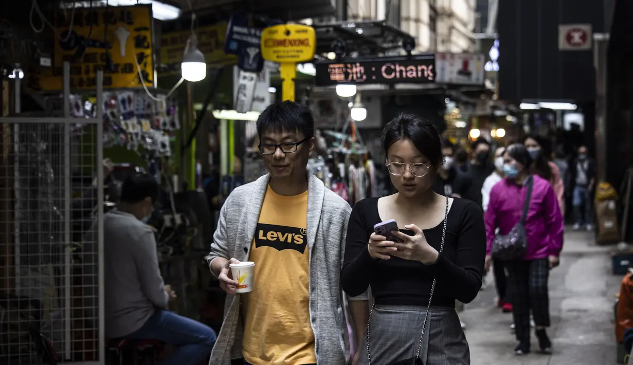 Pasangan berjalan melalui kawasan pusat bisnis di Hong Kong (1/3/2023). Sebelumnya, Hong Kong termasuk negara dengan aturan Covid yang sangat ketat. Mereka akan mendenda siapapun yang tidak mengenakan masker hingga wajib karantina atau isolasi di hotel hingga 21 hari. (AFP/Isaac Lawrence)