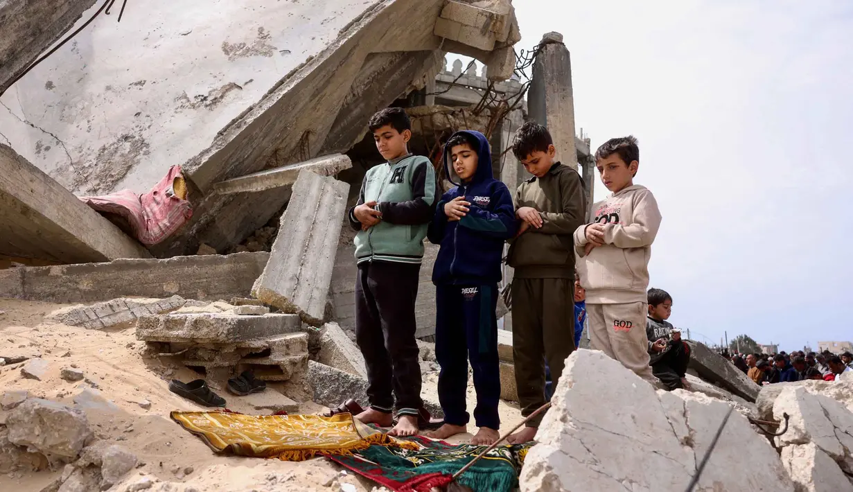 Pemandangan memilukan terlihat saat ratusan warga Palestina, termasuk anak-anak, berkumpul untuk melaksanakan salat Jumat di antara puing-puing masjid yang hancur akibat serangan Israel. Tampak dalam foto, anak-anak muda Palestina berdoa saat salat Jumat terakhir di bulan suci Ramadan 1447 Hijriah, di luar Masjid Al-Talbani, yang dihancurkan oleh militer Israel di Khan Yunis, Jalur Gaza selatan pada Jumat 13 Maret 2026. (Bashar Taleb/AFP)