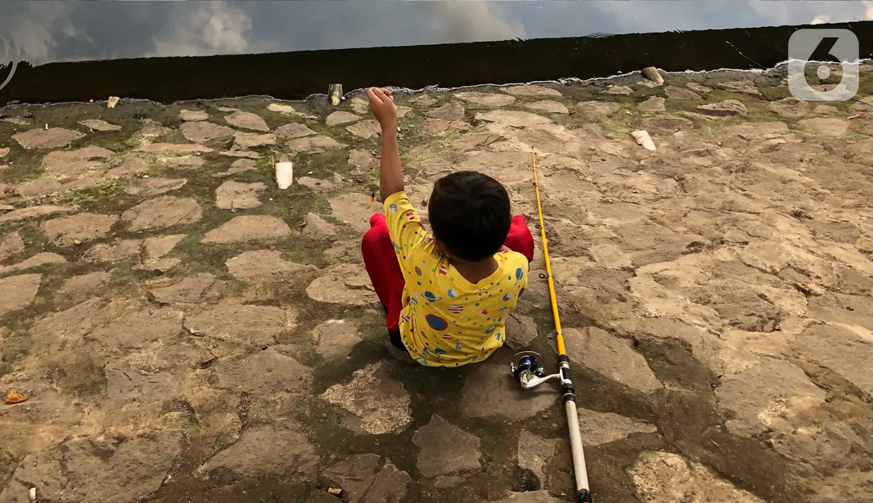 Seorang anak memancing ikan di kubangan yang berada di Jalan DI Panjaitan, Jatinegara, Jakarta, Selasa (16/6/2020). Meski telah dipagari, sejumlah warga tetap memancing ikan di lokasi yang merupakan saluran pembuangan tersebut. (Liputan6.com/Immanuel Antonius)