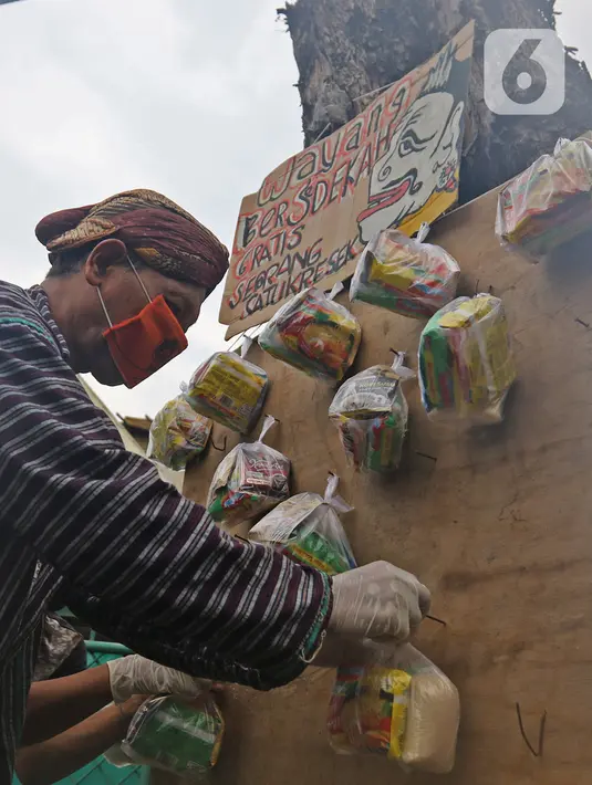 Seniman wayang uwuh, Iskandar Hardjodimuljo menggantungkan paket bahan makanan di jalan Cawang Baru Utara, Jakarta, Sabtu (18/4/2020). Paket sembako gratis itu inisiatif untuk menyisihkan hasil penjualan wayang uwuh yang terbuat dari sampah plastik dan kardus bekas. (Liputan6.com/Herman Zakharia)