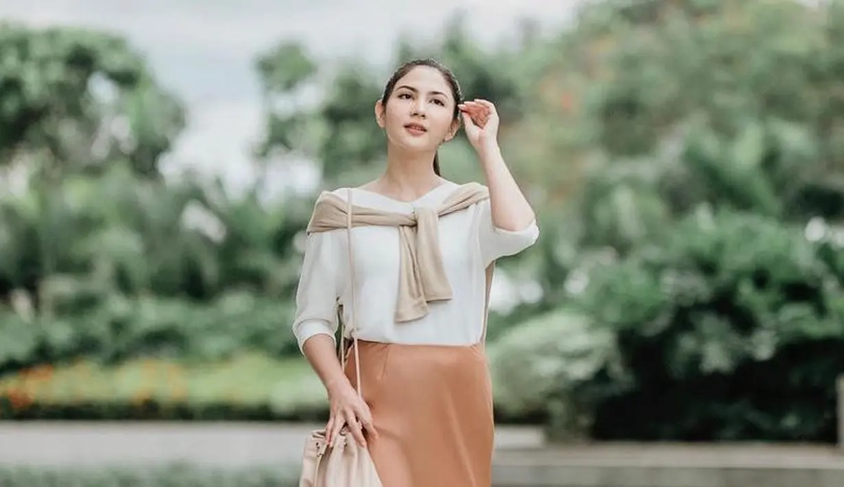 Tampilan feminin yang stylish, padukan long sleeve dengan satin flare skirt warna peach. Makin stylish dengan cardigan yang diikat di pundak. (Instagram/jscmila).