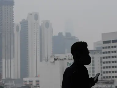 Seorang pria mengenakan masker saat kabut menyelimuti gedung-gedung di Kuala Lumpur (10/9/2019). Malaysia tengah mempersiapkan membuat hujan buatan setelah kualitas udara di sejumlah negara bagian mencapai level yang tidak sehat. (AFP Photo/Mohd Rasfan)