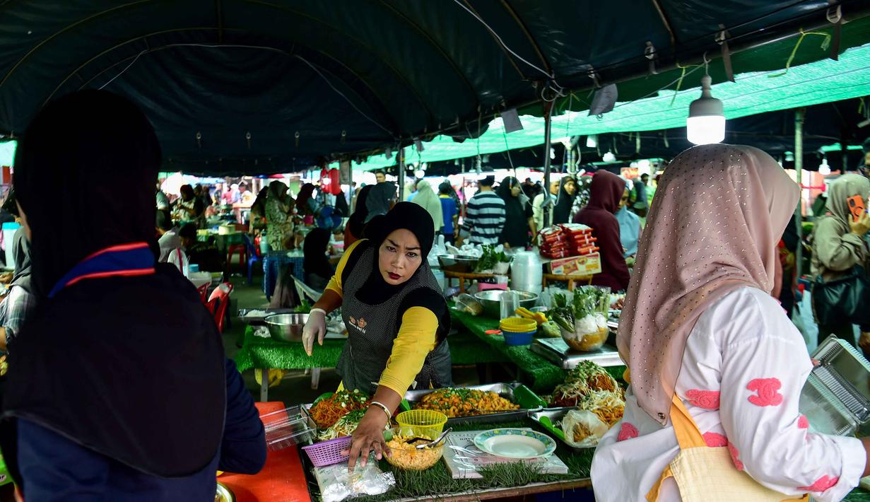 Pasar-pasar ini menawarkan beragam hidangan yang sulit ditemukan di luar bulan Ramadan. Tampak dalam foto, seorang pedagang kaki lima yang menjual makanan untuk berbuka puasa mendirikan lapaknya pada hari pertama bulan suci Ramadan 1447 Hijriah di sebuah pasar di provinsi Narathiwat, Thailand selatan, pada Kamis 19 Februari 2026. (Madaree TOHLALA/AFP)