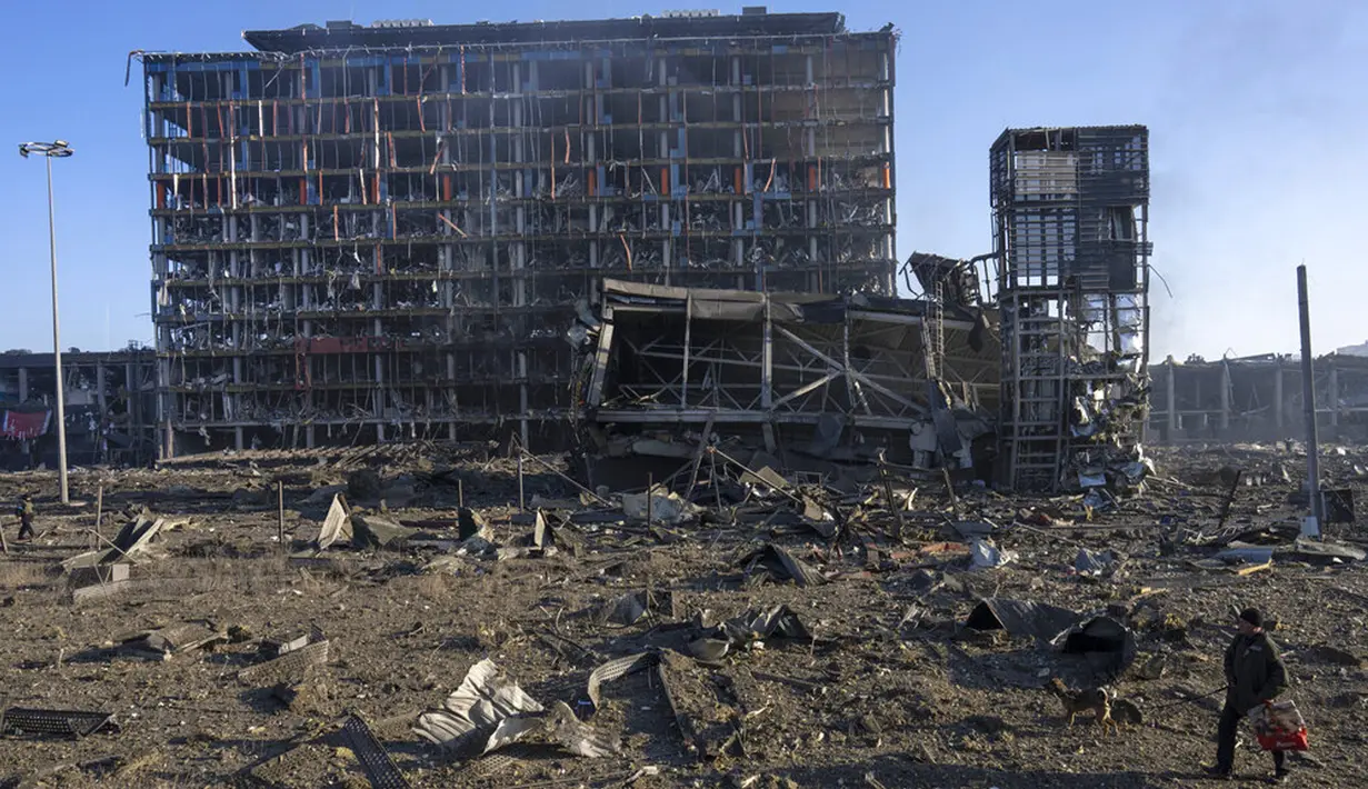 Seorang pria berjalan dengan anjingnya di tengah kehancuran setelah serangan sebuah pusat perbelanjaan di Kiev, Ukraina, Senin (21/3/2022). Delapan orang tewas dalam serangan tersebut. (AP Photo/Rodrigo Abd)
