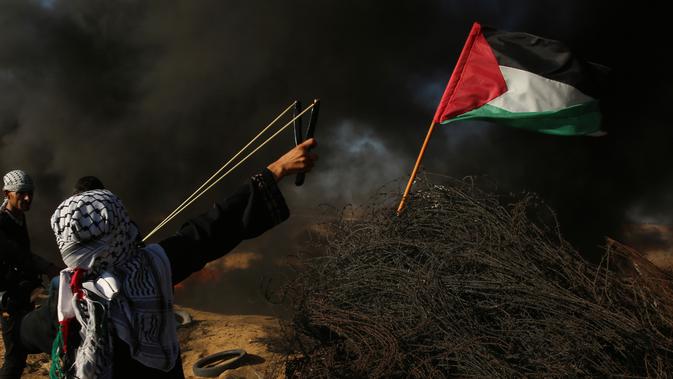 Pengunjuk rasa wanita Palestina menembakkan batu menggunakan ketapel ke arah tentara Israel saat bentrok di Khan Younis, perbatasan Gaza, Jumat (10/8). (AP Photo/Adel Hana)
