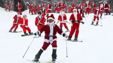 Pemain ski dan snowboarder berpakaian Santa Claus menuruni lereng gunung saat Santa Sunday ke-19 di Newry, Maine, AS, Minggu (2/12). Lebih dari 200 Santa menuruni lereng gunung secara massal dalam acara Santa Sunday tahun ini. (AP Photo/Robert F. Bukaty)