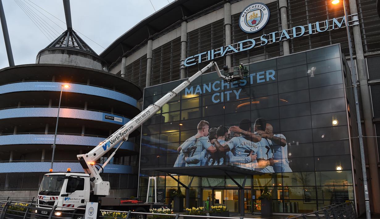 Pekerja memasang poster raksasa bergambar pemain Manchester City terpasang di Stadion Etihad, Manchester, Senin (17/4/2018). Persiapan ini dilakukan untuk merayakan pesta juara Manchester City meraih gelar Premier League. (AFP/Paul Ellis)