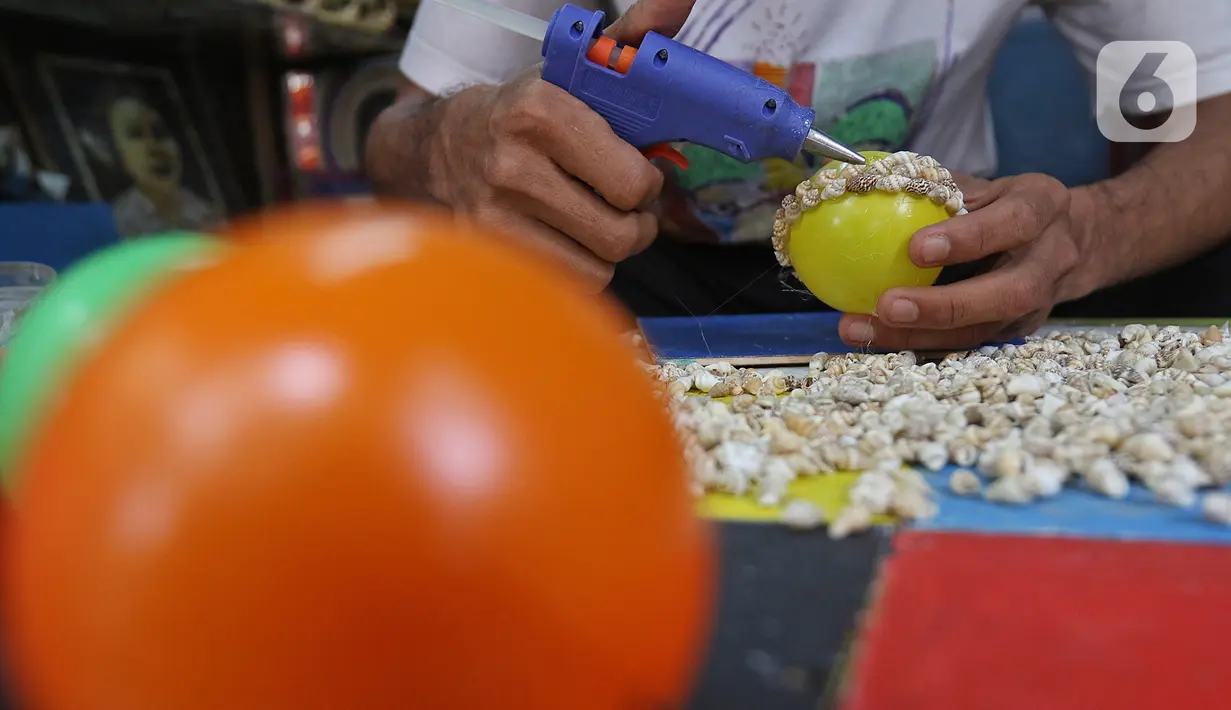 Perajin membuat kerajinan dari limbah kerang di Kawasan Ancol Jakarta, Kamis (14/11/2019). Sejak 2008, Sugiro (39) telah melakoni pemanfaatan limbah kerang untuk dibuat menjadi berbagai kerajinan seperti bola dihiasi kerang, pigura, helm, hiasan dinding dan baju adat. (Liputan6.com/Herman Zakharia)