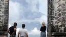 Wisatawan melihat asap Gunung Agung di sebuah kuil di Kabupaten Karangasem, Bali, (27/11). Pihak berwenang telah mengantisipasi dampak yang ditimbulkan oleh aktivitas Gunung Agung dengan menutup Bandara Ngurah Rai. (AP Photo / Firdia Lisnawati)