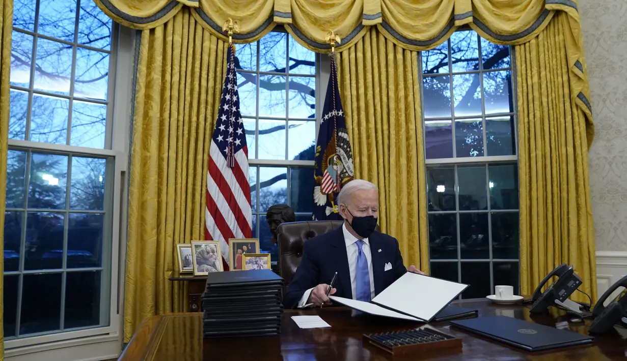 Presiden Joe Biden menandatangani perintah eksekutif pertamanya di Ruang Oval, Gedung Putih di Washington, Rabu (20/1/2021). Pada hari pertamanya menjabat, Presiden Amerika Serikat Joe Biden menandatangani sejumlah tindakan eksekutif di Gedung Putih. (AP Photo/Evan Vucci)