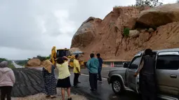 Orang-orang melihat batu-batu besar di jalan raya menuju bandara Narathiwat menyusul tanah longsor setelah hujan lebat di Thailand selatan (25/11/2019). Wilayah selatan Thailand akan memasuki musim hujan lebat tiga bulan dari November hingga Januari. (AFP/Madaree Tohlala)