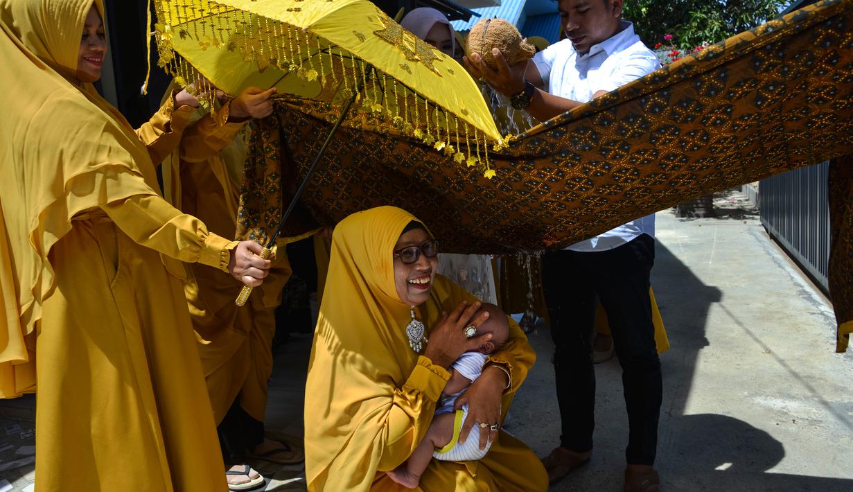 Tokoh adat dan agama mengendong bayi saat orang tua (ayah bayi) membelah kelapa pada ritual 'peutron tanoh aneuk' (turun tanah anak) di Banda Aceh, Aceh, Senin (15/7/2019). Ritual turun tanah anak dilaksanakan pada saat bayi berusia 44 hari. (CHAIDEER MAHYUDDIN / AFP)