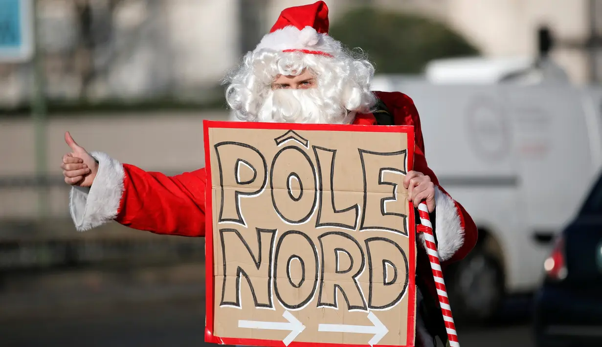 Seorang petualang asal Prancis, Remi Le Calvez membawa poster bertuliskan 'Pole Nord' yang artinya kutub utara, mencari tumpangan kendaraan dengan mengenakan kostum Santa Claus di Paris, Prancis, Selasa (6/12). (Reuters/Benoit Tessier)