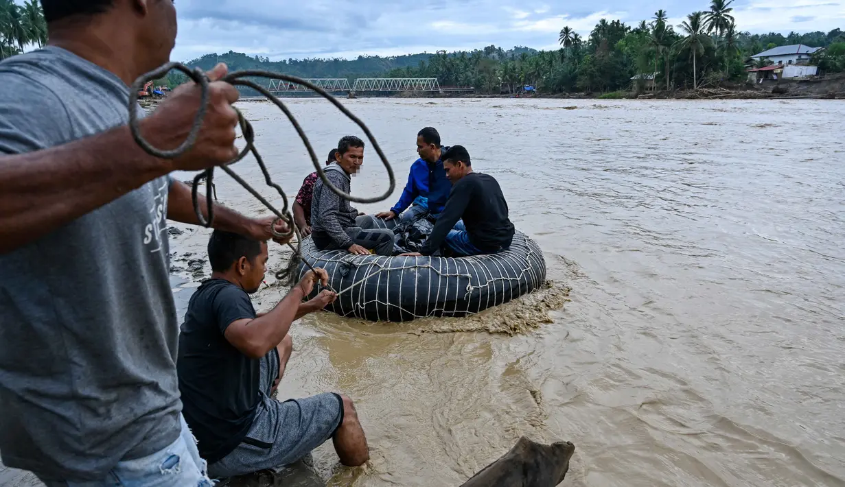Pembangunan jembatan darurat sangat penting agar mobilitas masyarakat setempat dapat kembali berlangsung dengan normal. Tampak dalam foto, warga menggunakan ban dalam sebagai perahu darurat untuk menyeberangi sungai setelah jembatan rusak akibat banjir di Juli, provinsi Aceh, pada Minggu 14 Desember 2025. (CHAIDEER MAHYUDDIN/AFP)