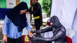 Petugas Kelompok Penyelenggara Pemungutan Suara (KPPS) berkostum superhero Venom membantu warga mencelupkan jari ke tinta dalam Pemilu 2019 di sebuah TPS di Surabaya, Jawa Timur, Rabu (17/4). Petugas KPPS berharap menarik pemilih, khususnya milenial. (Juni Kriswanto/AFP)