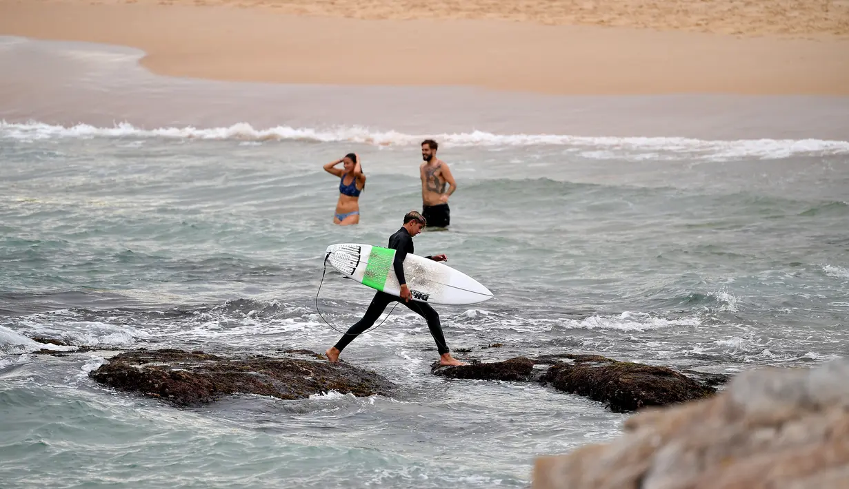 Seorang pria membawa papan selancar saat pembatasan sosial diberlakukan di Pantai Maroubra di Sydney, Australia (20/4/2020). (AFP/Saeed Khan)