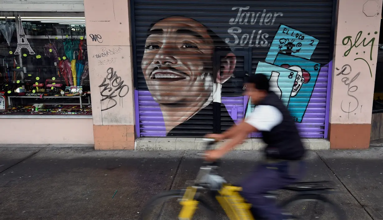 Pengendara sepeda melintas di depan mural penyanyi Javier Solis yang menghiasi pintu toko di Mexico City, Meksiko, 30 Agustus 2017. Mural menjadi salah satu langkah Pemerintah Mexico City melestarikan dan mempercantik ruang publik. (ALFREDO ESTRELLA/AFP)