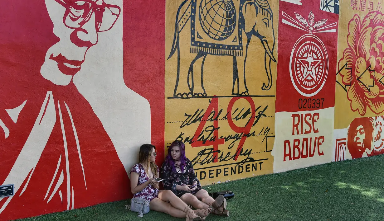 Dua orang wanita duduk di dekat mural yang dibuat oleh seniman Shepard Fairey di kawasan Wynwood, Miami, Florida pada 28 September 2016. Goldman Properties menggelar pameran mural untuk merevitalisasi lingkungan. (AFP PHOTO / Rhona WISE)