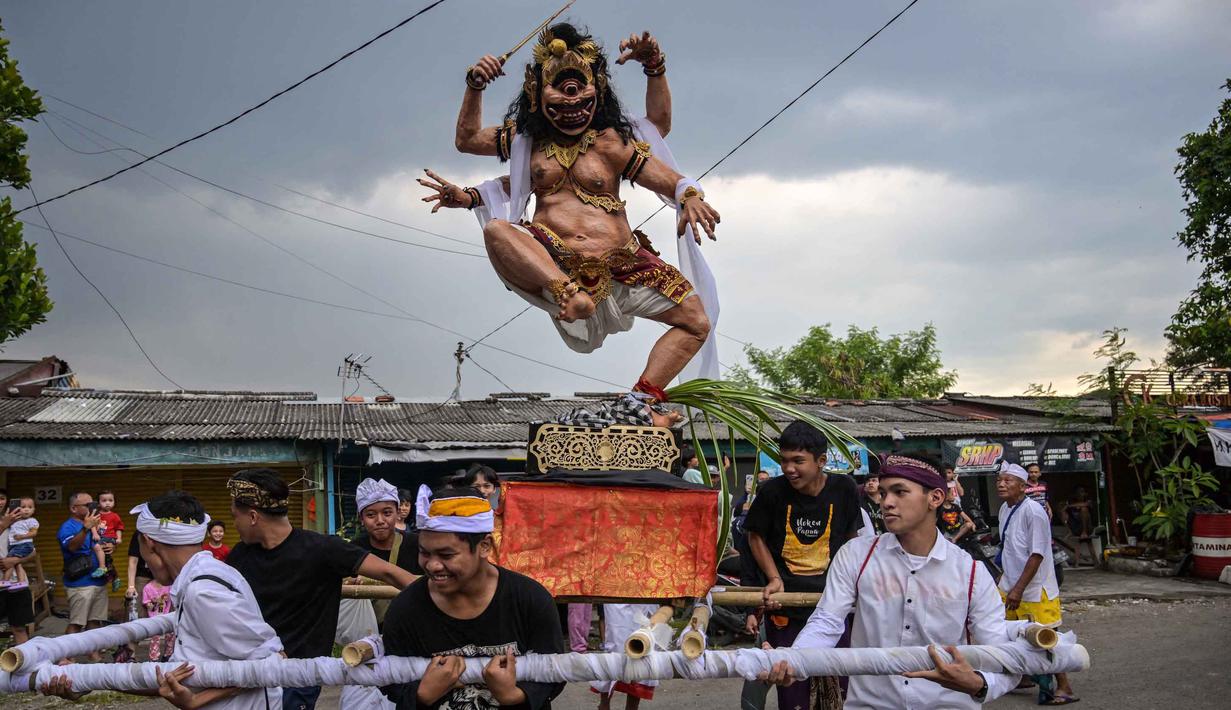 Bhuta Kala merepresentasikan kekuatan alam semesta dan waktu yang tak terhingga, yang divisualisasikan dalam bentuk raksasa atau makhluk menyeramkan sebagai simbol energi negatif atau kejahatan. Tampak dalam foto, para penganut Hindu membawa Ogoh-ogoh, patung yang melambangkan roh jahat, selama pawai menjelang Nyepi di Surabaya pada Rabu 18 Maret 2026. (JUNI KRISWANTO/AFP)