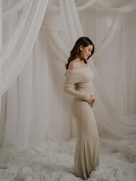Dalam salah satu unggahannya, Aaliyah tampak memesona dalam balutan off-shoulder dress berwarna soft beige. Dress berbahan knit ini membentuk lekuk tubuhnya dengan sempurna, menonjolkan baby bump dengan anggun. [@aaliyah.massaid].