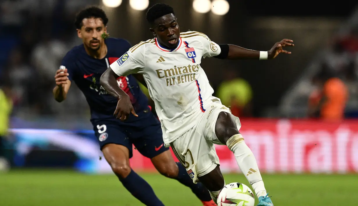 Bek Paris Saint-Germain (PSG) #05 Marquinhos berebut bola dengan penyerang Lyon #37 Ernest Nuamah pada laga pekan keempat Ligue 1 2023/2024 di Groupama Stadium, Senin (04/09/2023) dini hari WIB. (Photo by Jeff PACHOUD / AFP)