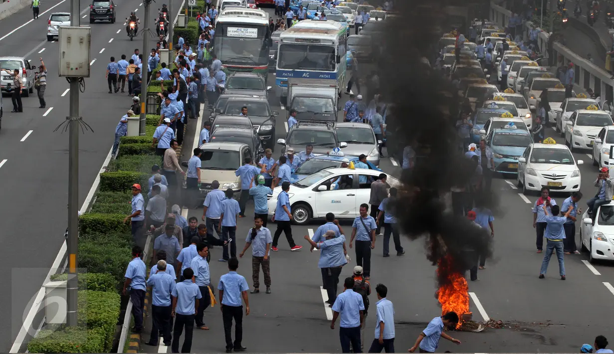 Sejumlah sopir taksi yang melakukan demo membakar ban dan memblokir jalan di tol dalam kota, Mampang, Jakarta, Selasa (22/3). Terlihat asap membumbung tinggi dari ban yang terbakar. (Liputan6.com/Johan Tallo)