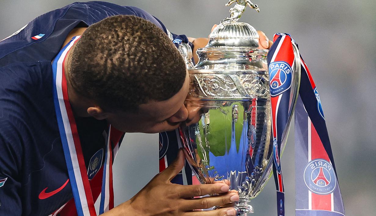 Pemain PSG, Kylian Mbappe mencium trofi Coupe De France 2023/2024 saat upacara penyerahan di Stade Pierre-Mauroy, Villeneuve-d'Ascq, Prancis, Minggu (26/05/2024) WIB. PSG menang dengan skor 2-1 atas Olympique Lyon pada babak final. (AFP/Denis Charlet)