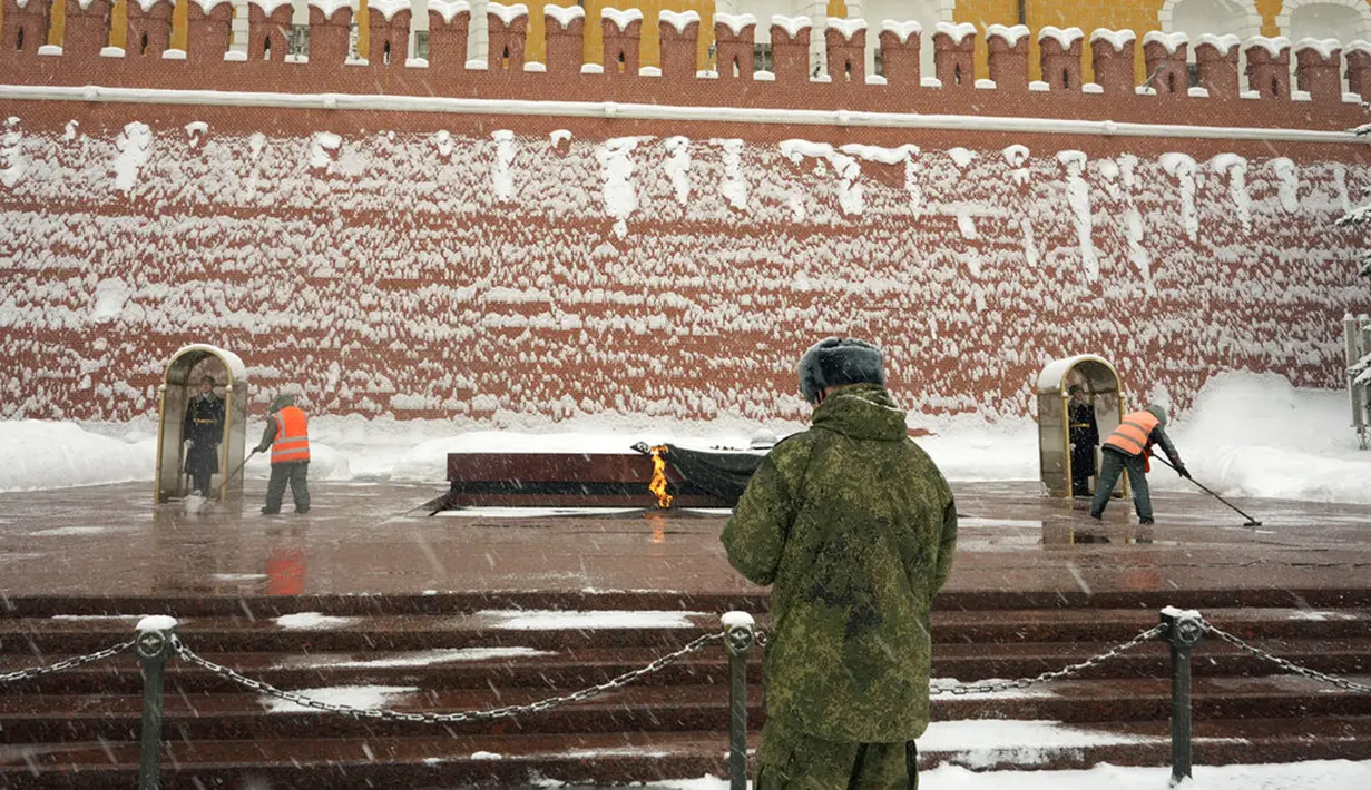 Para pekerja membersihkan salju dari Makam Prajurit Tak Dikenal yang dijaga sejumlah prajurit di Tembok Kremlin, Moskow, Rusia, 7 Februari 2022. (AP Photo/Thibault Camus)