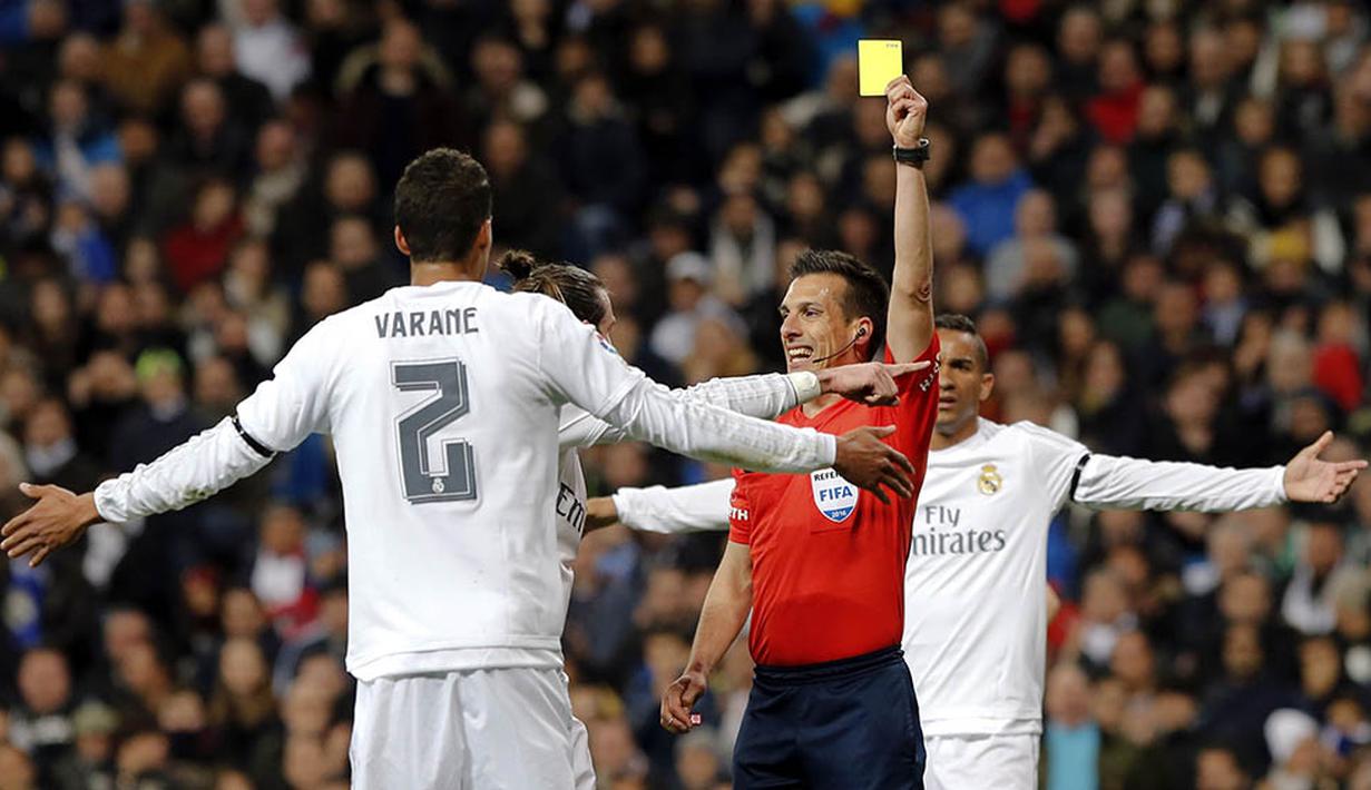 Wasit Estrada Fernandez memberikan kartu kuning kepada bek Real Madrid, Raphael Varane, pada laga La Liga Spanyol melawan Sevilla di Stadion Santiago Bernabeu, Madrid, Minggu (20/3/2016). Madrid menang 4-0 atas Sevilla. (EPA/Ballesteros)