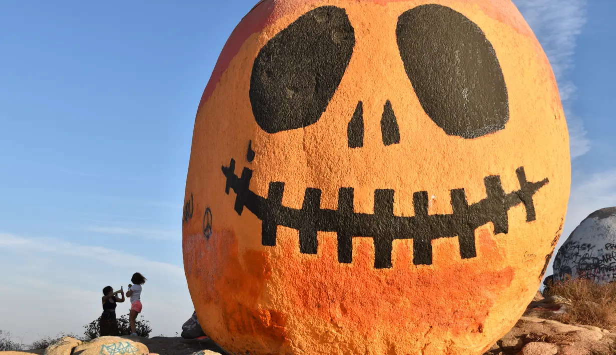 Orang-orang mengunjungi Pumpkin Rock (Batu Labu) di puncak sebuah bukit di Norco,  California, AS (18/10/2020). Menjelang perayaan Halloween, Pumpkin Rock, sebongkah batu raksasa yang dilukisi seperti Jack-O'-Lantern besar, menjadi objek wisata yang populer bagi pengunjung. (Xinhua/Gao Shan)